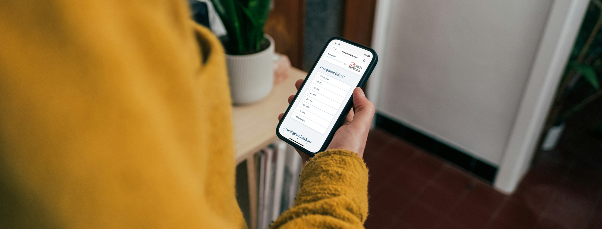 Bilden visar en person som håller i en mobiltelefon med Glada Hudikhems hyresgästundersökning på sk