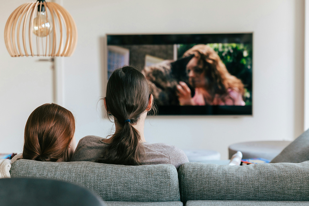Bilden visar två personer som sitter i en soffa och tittar på TV